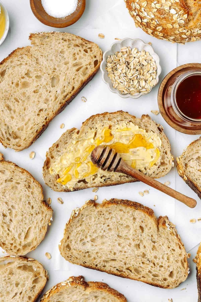 honey being drizzled over a buttered piece of honey oatmeal sourdough bread
