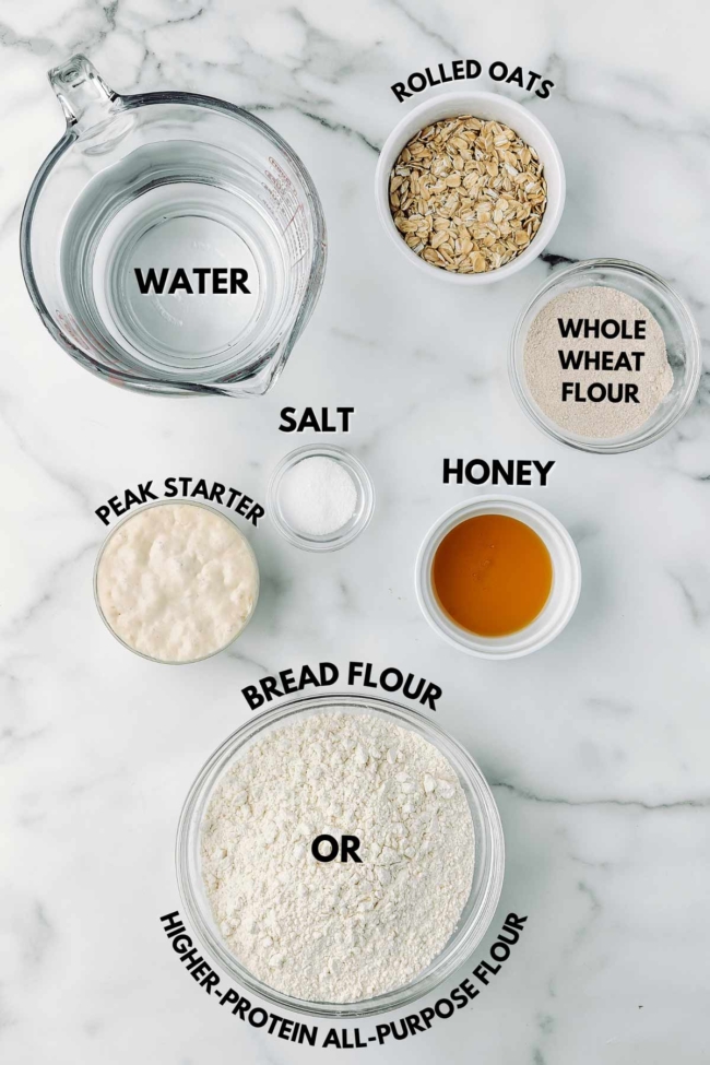 ingredients laid out to make honey oat sourdough on a marble table