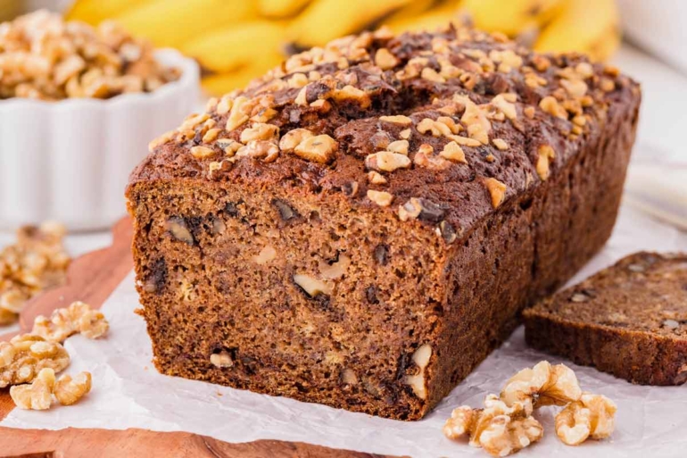 Sliced loaf of whole wheat banana nut bread with walnuts on top