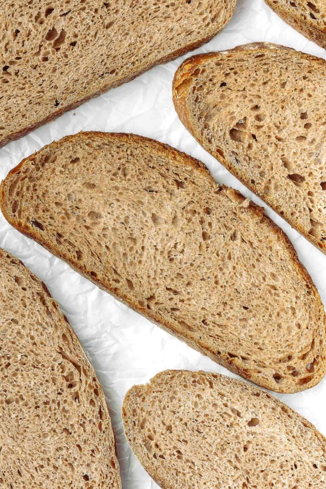 Sliced whole wheat sourdough bread showcasing its crumb and crust on a white background.