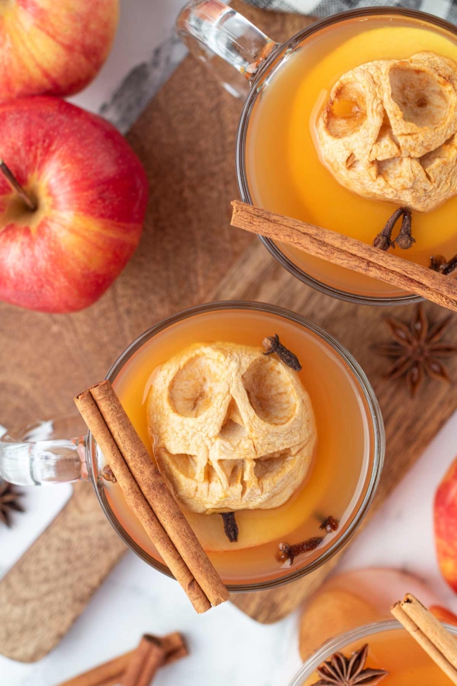 Warm spiced apple cider topped with a carved shrunken apple head and garnished with cinnamon sticks and cloves.