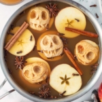 Spooky apple skulls float in spiced cider with cinnamon sticks and star anise, creating a festive autumn display.