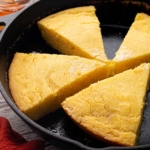 Golden sourdough cornbread cut into wedges in a cast iron skillet