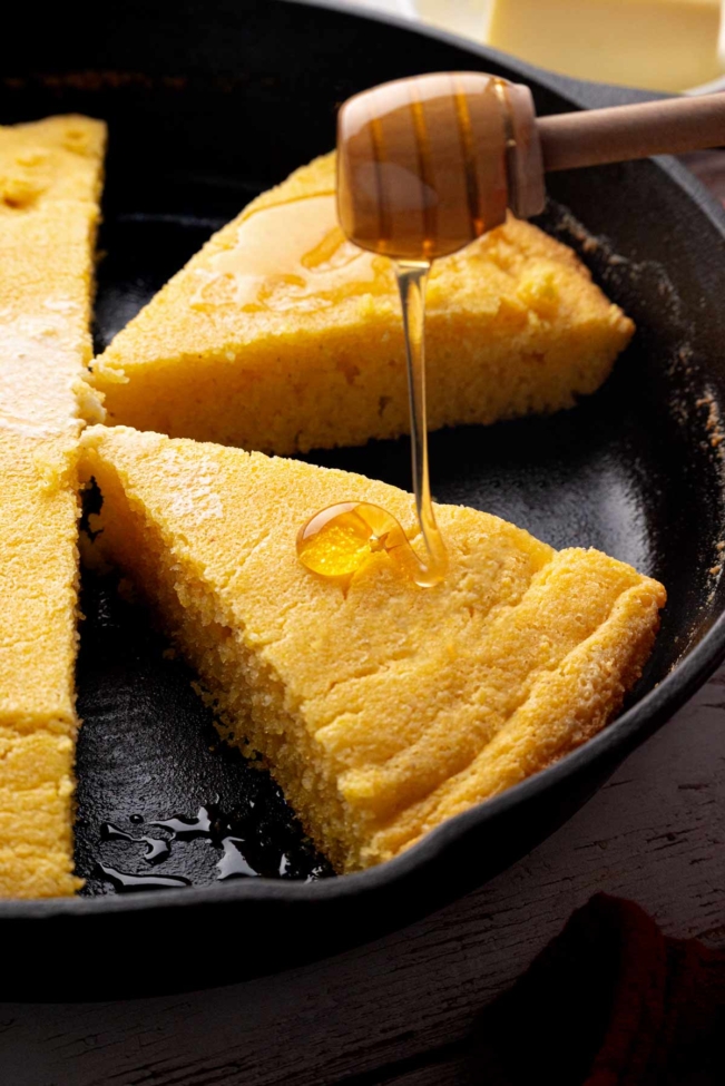 Honey being drizzled over a slice of sourdough discard cornbread