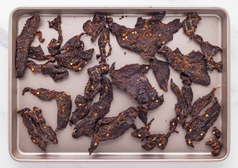 A tray of seasoned venison jerky pieces, showcasing a rich, dark color and a sprinkle of spices.