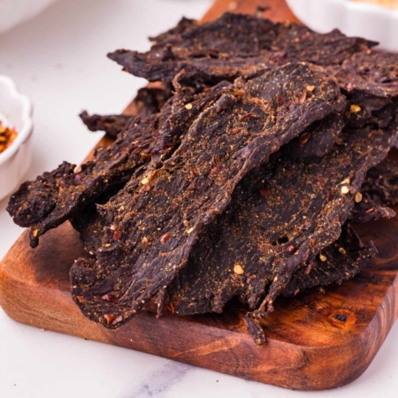Savory venison jerky strips seasoned with spices, displayed on a wooden cutting board.