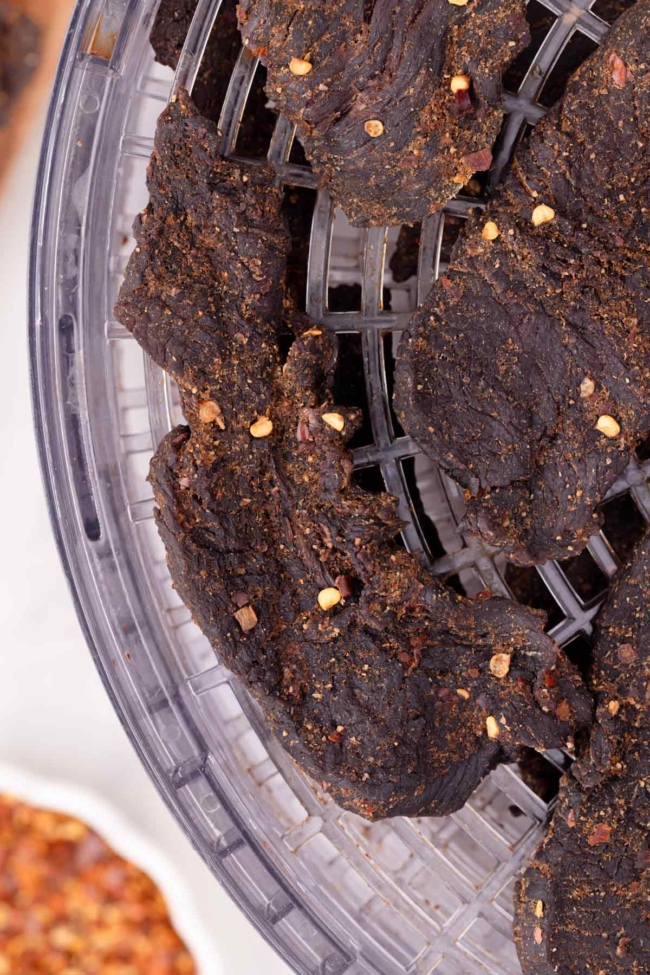 Close-up of seasoned venison jerky pieces drying on a tray, showcasing their rich texture and spices.