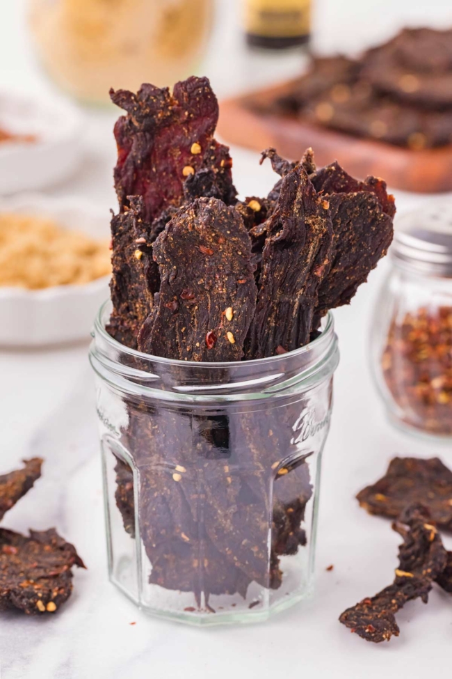 Venison jerky sticks are displayed in a glass jar, showcasing their rich color and seasoning.