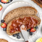 Whole wheat sourdough bread slice topped with jam, surrounded by fresh strawberries and blueberries on a plate.