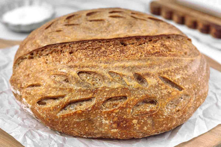 Crusty whole wheat sourdough bread with decorative scoring, resting on parchment paper.