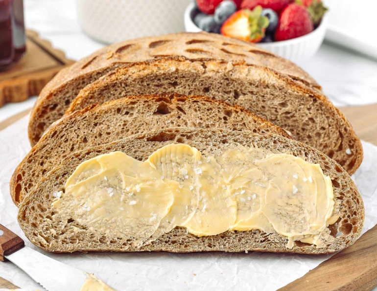 Sliced whole wheat sourdough bread spread with butter, showcasing its texture and crust.